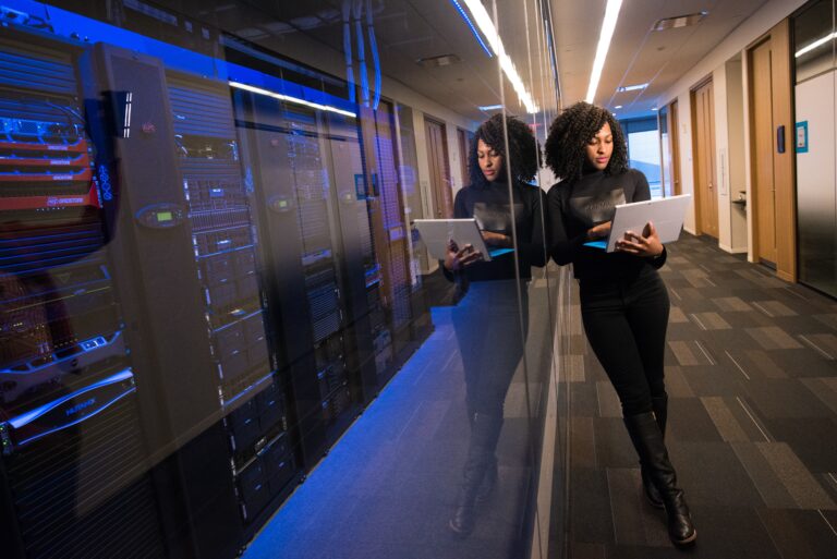Women typing on computer next to technology room.